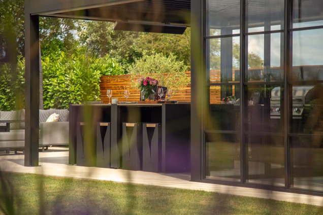 A photo looking through out-of-focus lavender towards a Grillo outdoor kitchen under a pergola in Attleborough
