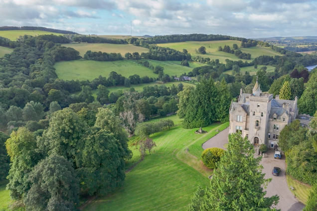 A drone photo looking along the Tweed Valley, with a Baronial turreted mansion in the foreground