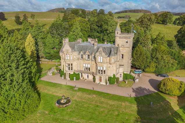 A drone photo of a castle in the Scottish Borders with rolling hills in the background, all bathed in sunlight