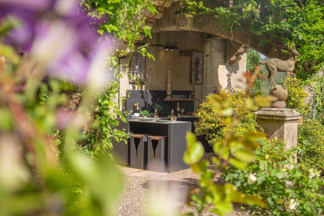 Looking towards a Grillo kitchen at a Baronial mansion, with the view framed by out-of-focus purple flowers to one side and stag-and-ball-finialled balusters of the double perron stairway to the other