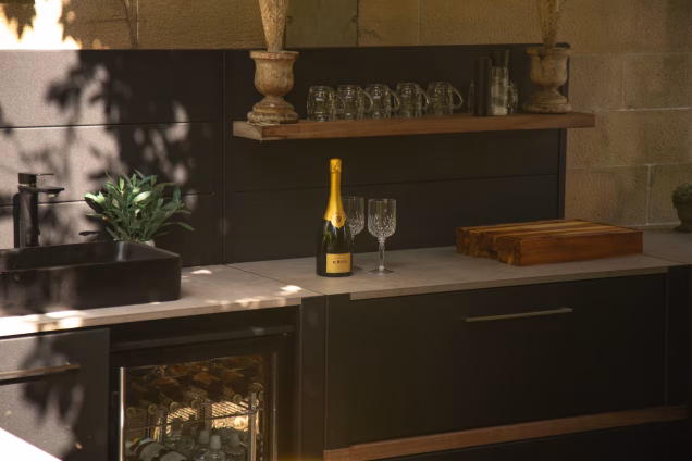 Atmostpheric, dark and gold-hued photo of a bottle of Krug champagne in a Grillo kitchen against the dressed sandstone blocks of a castle wall