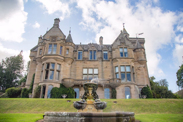 The south eastern elevation of a castle in the Scottish Borders, displaying a number of Scottish Baronial architectural features, with a fountain in the foreground