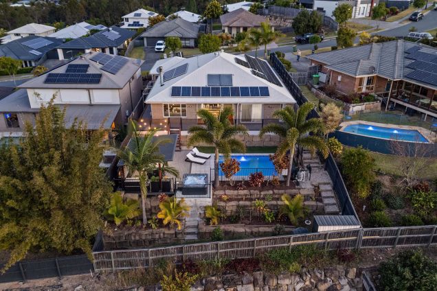 drone shot looking at garden with pool, grillo outdoor kitchen, and hot tub on decking