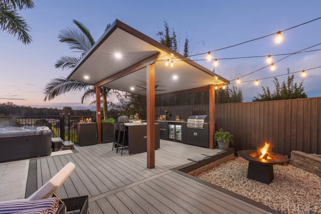 outdoor kitchen under large wooden cover on decking with firepit area