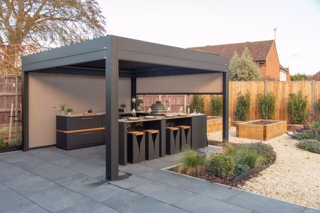 A wide angle view of a Grillo Pergola and outdoor kitchen in a garden with laurels along the back fence
