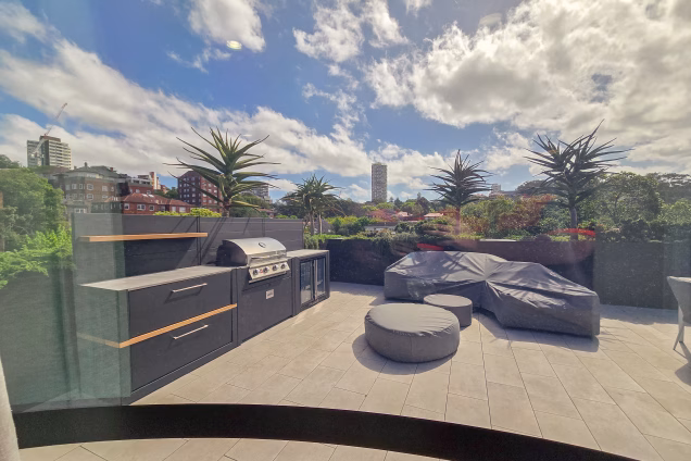 The view out of a curved glass facade from a penthouse office across the roof terrace featuring an outdoor kitchen