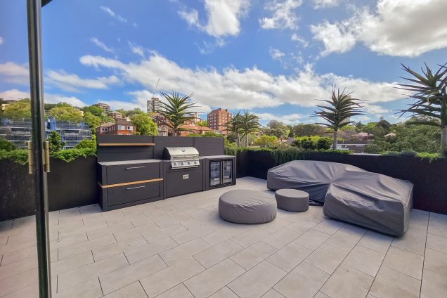 A view of an outdoor kitchen featuring a powerful Bull gas grill and an outdoor double fridge on a Sydney roof terrace