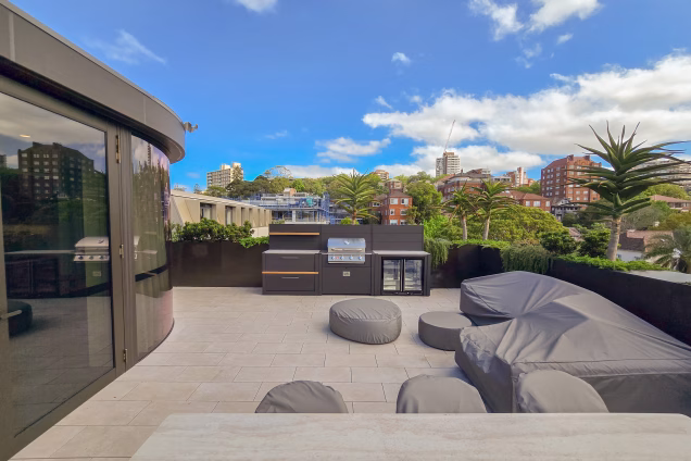 A wide angle view of a Double Bay roof terrace, featuring covered furniture and a Grillo outdoor kitchen