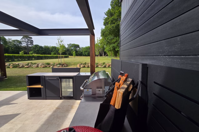 A closeup photo looking along a run of outdoor kitchen over a Bull gas grill to the landscaped garden beyond