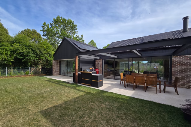 A view of the back of a modern, new-build property in Moss Vale NSW, featuring and outdoor kitchen and dining area on a patio
