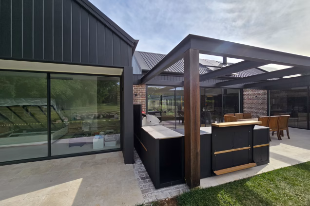 The back of a house in Moss Vale with a modern dark metal and brick exterior, and a lot of glass doors leading to the garden