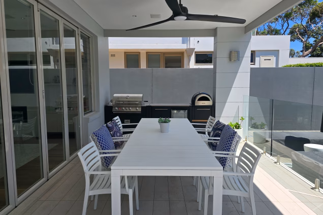 Looking along the dining table towards the outdoor kitchen at a contemporary property overlooking the Sutherland Shire bays