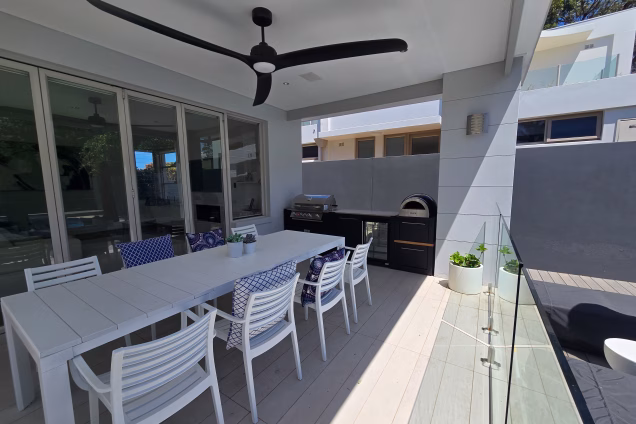 A wide angle view of the alfresco at this Sydney property, featuring a white dining table and chairs, and a black Grillo outdoor kitchen