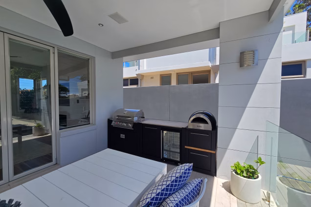An outdoor kitchen and dining area in an impressive white-rendered property in Sydneys bayside Burraneer suburb