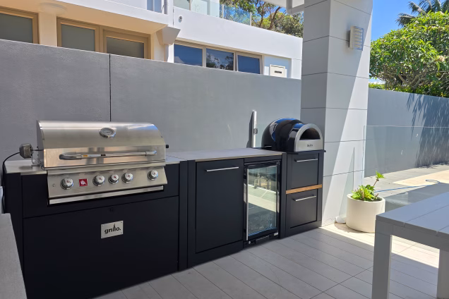 Looking along a Grillo outdoor kitchen with gas grill and pizza oven, with native trees in the background