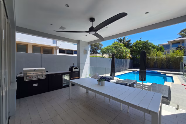 The view across the alfresco and garden of a property by Burraneer Bay, featuring a pool and outdoor kitchen and dining set