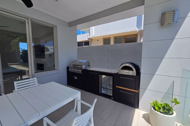A Grillo outdoor kitchen tightly fitting between a house wall and column in an alfresco area, featuring a powerful Bull Angus gas grill, a Delivita pizza oven and outdoor fridge