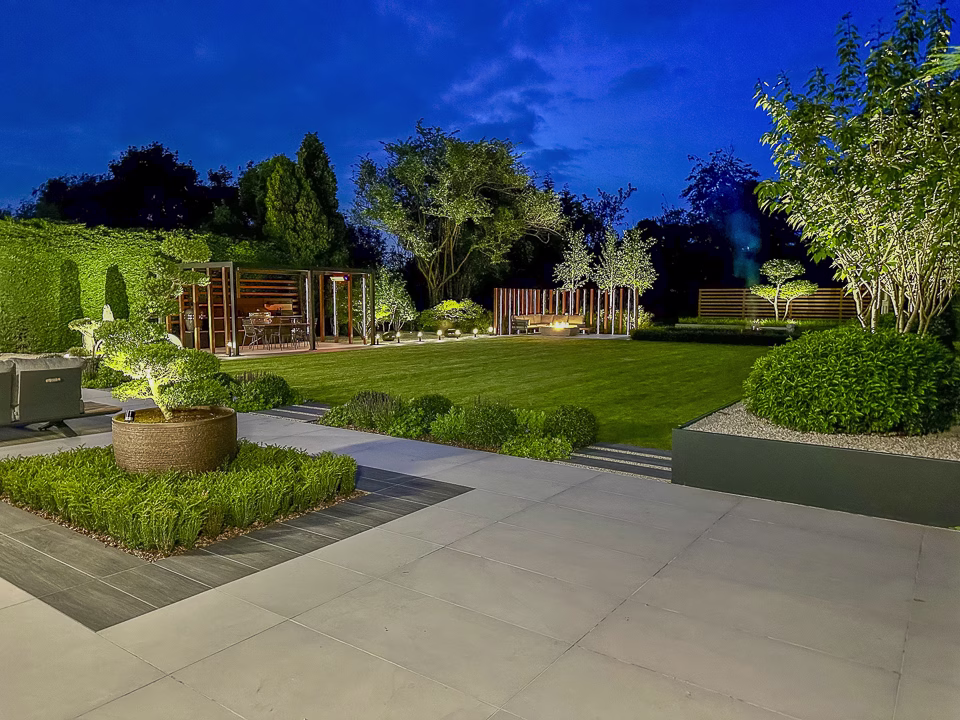 Overlooking a garden design that features a wrap around patio, seating areas, grass area, planting and an outdoor kitchen underneath a pergola