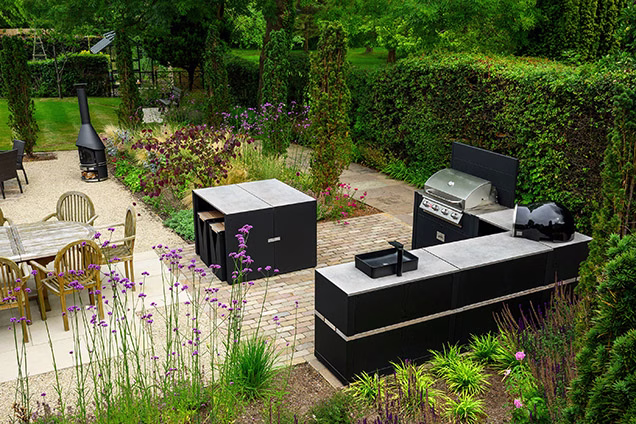outdoor kitchen on block paved patio with bar table and stools, bull gas grill station, pizza oven and sink and storage