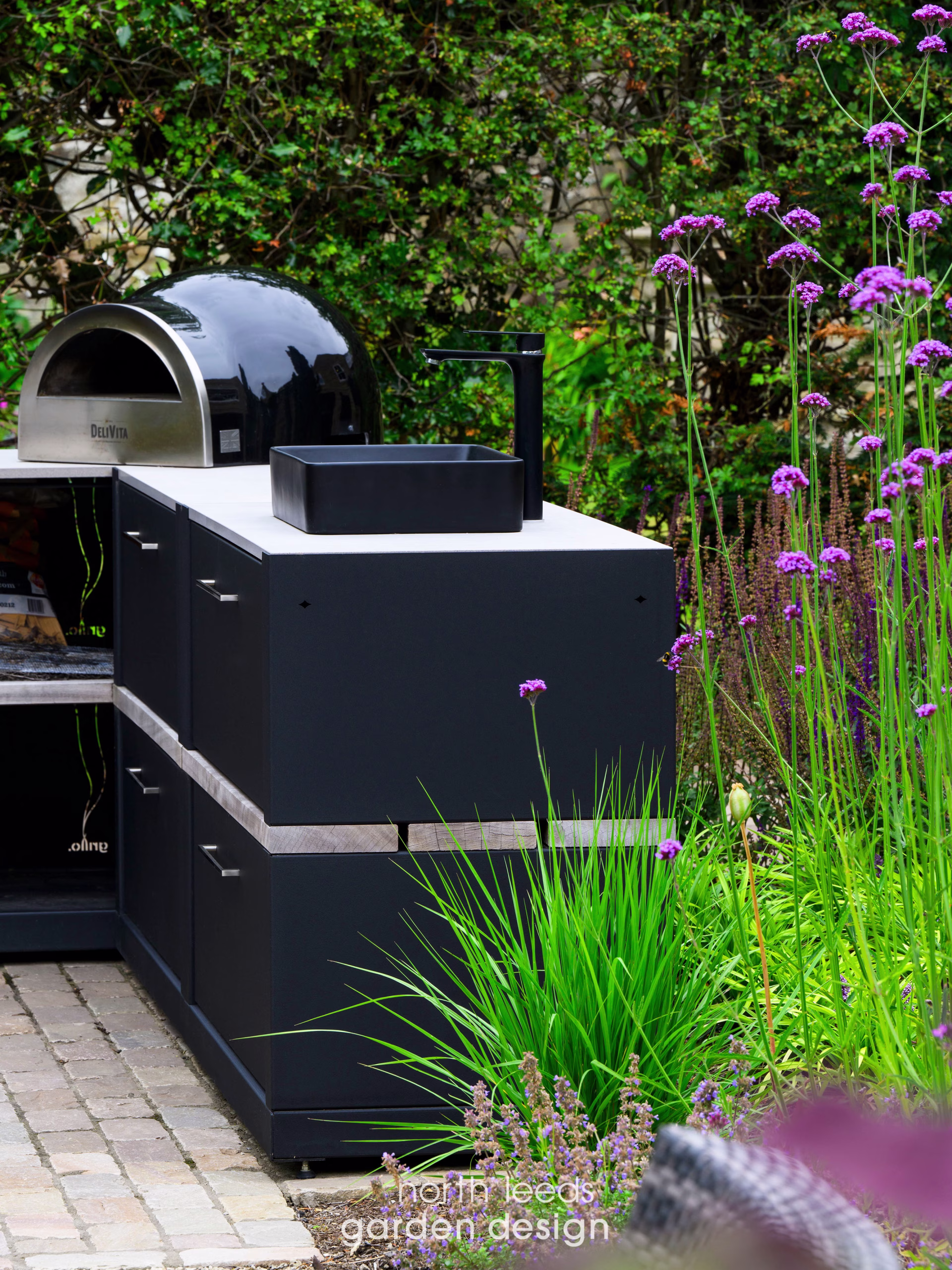 outdoor kitchen on block paving patio with pizza oven, sink and storage