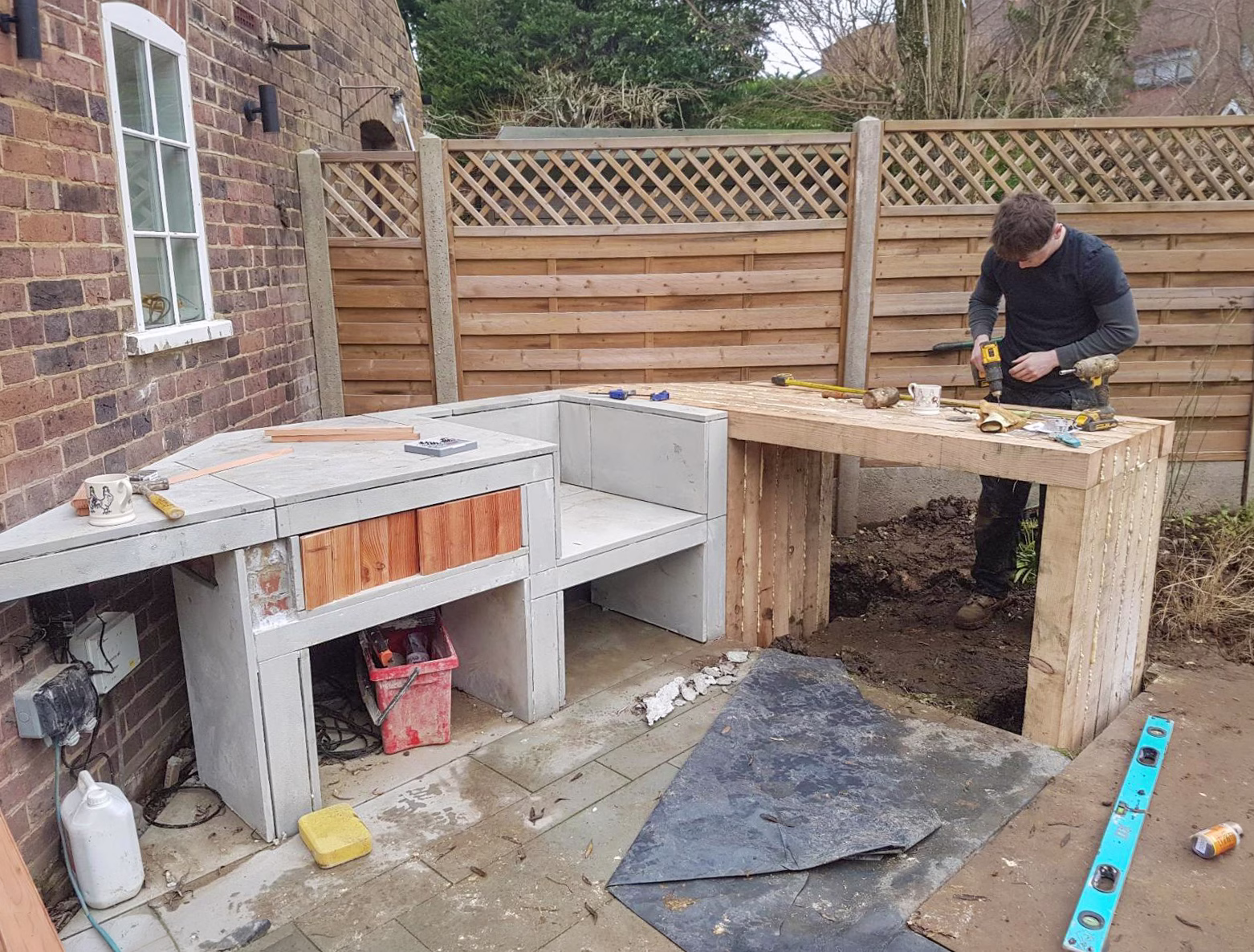 A custom outdoor kitchen being built by a tradesman, using custom brickwork, tilework, timberwork, and laid on concrete footings