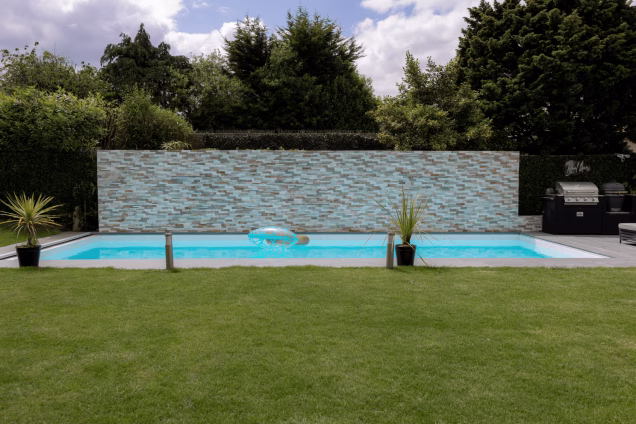 A view over a lawn with a large swimming pool and Grillo kitchen alongside