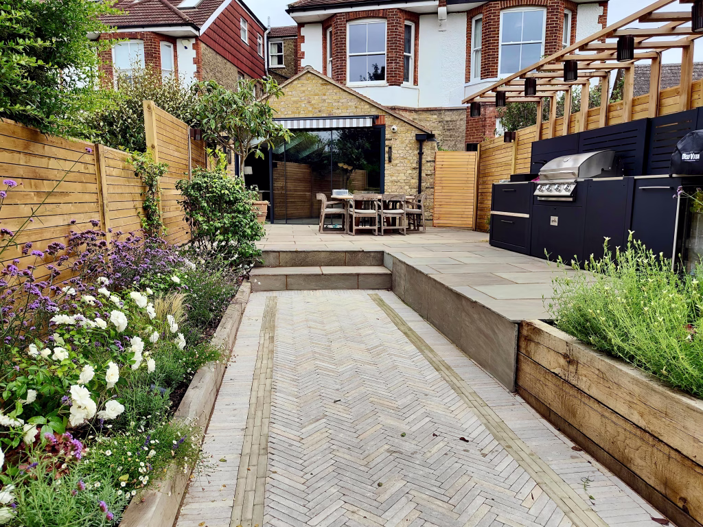 A narrow garden in London with a Grillo kitchen, featuring herringbone clay pavers and drought resistant planting
